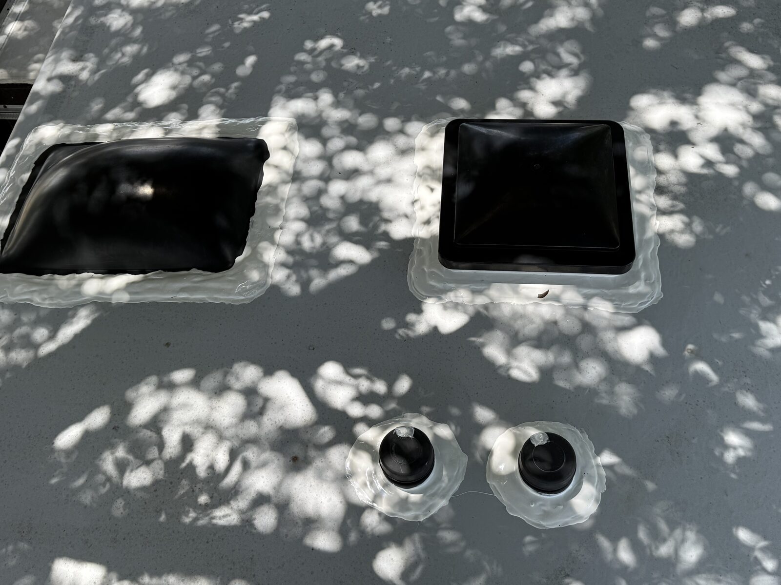 Two RV roof vent covers freshly sealed with black lap sealant